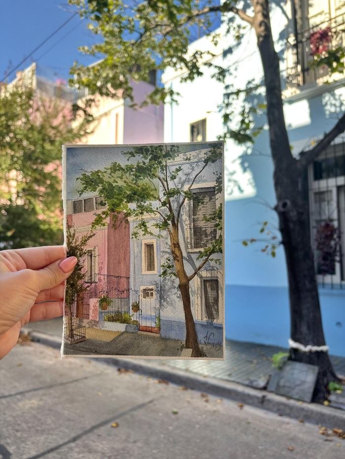 Paisaje urbano en acuarela, sostenido frente a la calle de casas de colores que retrata