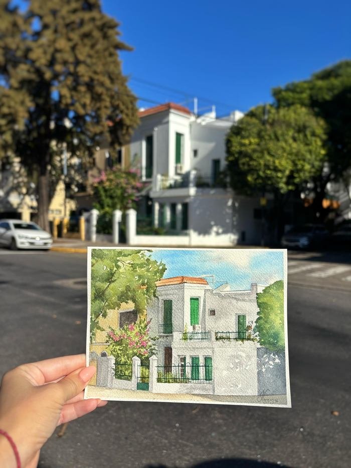 Acuarela de una casa con su jardín, sostenida frente a la esquina real